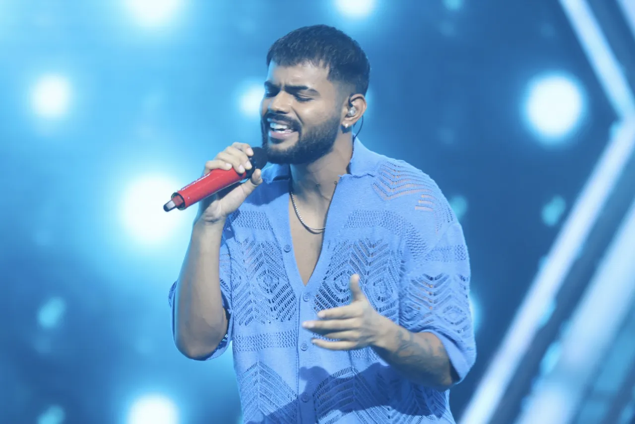 Badal singing into a red microphone on stage under blue lights