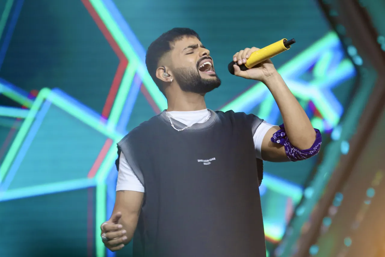 Badal performing with a yellow microphone in front of neon stage visuals