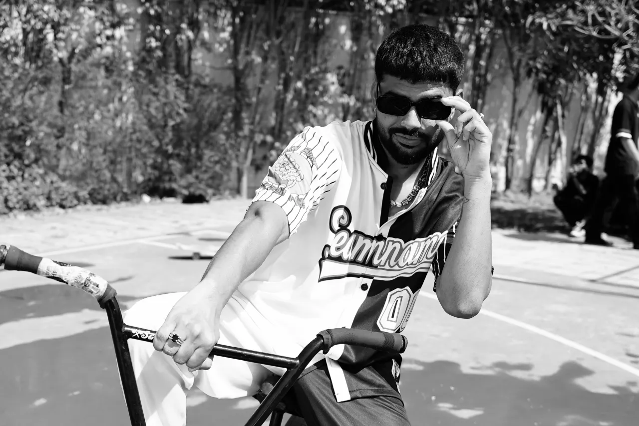 Black-and-white portrait of Badal on a bike, adjusting his sunglasses