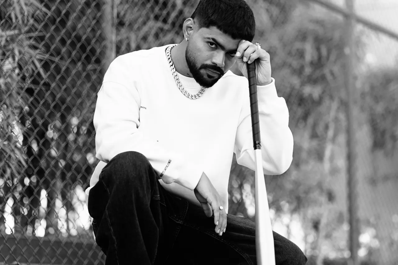 Black-and-white portrait of Badal crouching with a baseball bat by a chain-link fence